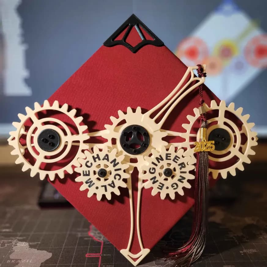 a maroon graduation cap with a series of gears on top. The tassle is attached to an arm extending from the central gear. The words mechanical engineering are spelled out across two gears